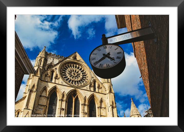 Vintage street clock hanging with a gothic cathedral facade in the background, showcasing intricate architecture and a clear blue sky in York, North Yorkshire, England. Framed Mounted Print by Man And Life