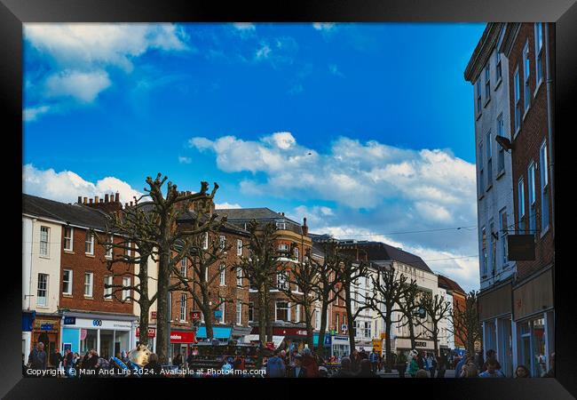 Bustling city street scene with pedestrians, unique pruned trees under a blue sky with clouds, and historic buildings, capturing the essence of urban life in York, North Yorkshire, England. Framed Print by Man And Life