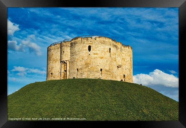 Medieval stone tower atop a lush green hill against a vibrant blue sky with fluffy clouds, symbolizing historical fortification and ancient architecture in York, North Yorkshire, England. Framed Print by Man And Life