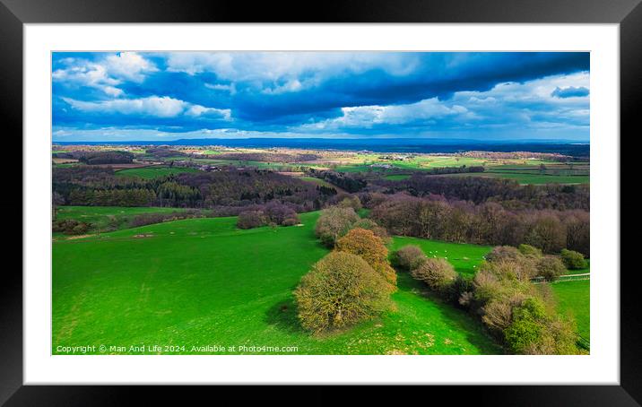 Vibrant aerial landscape with lush green fields, scattered trees, and a dramatic sky with fluffy clouds casting shadows over the countryside. Framed Mounted Print by Man And Life