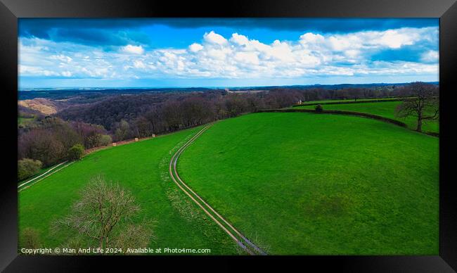 Scenic countryside landscape with lush green fields, a winding path, and a vibrant blue sky with scattered clouds. Ideal for backgrounds and nature themes. Framed Print by Man And Life