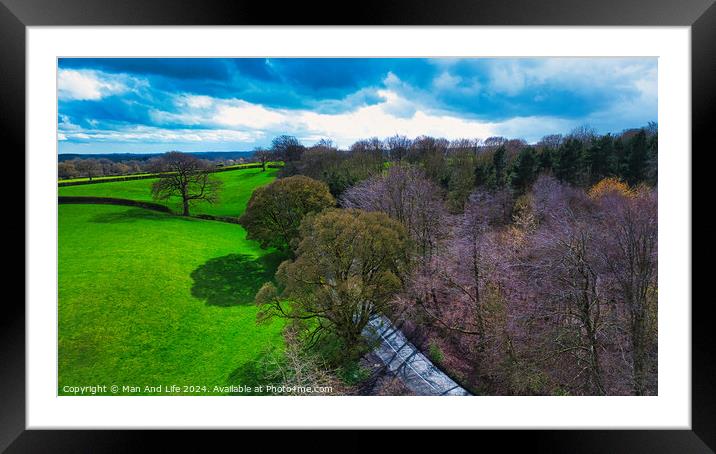 Aerial view of a vibrant countryside landscape with lush green fields, a meandering road, and a patch of bare trees under a dynamic sky with scattered clouds. Framed Mounted Print by Man And Life