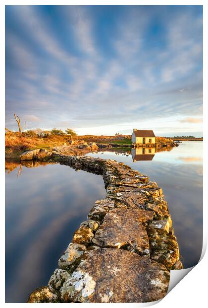 An old stone jetty across a lake leading to a small cottage Print by Helen Hotson