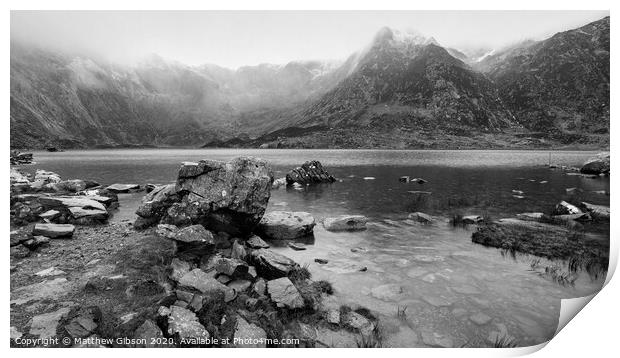 Beautiful moody Winter landscape image of Llyn Idwal and snowcapped Glyders Mountain Range in Snowdonia in black and white Print by Matthew Gibson