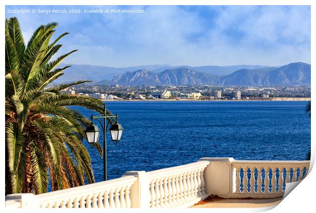 Beautiful seascape on the promenade, a street lamp under a palm tree looks at the sea, city and mountains in blur. Print by Sergii Petruk