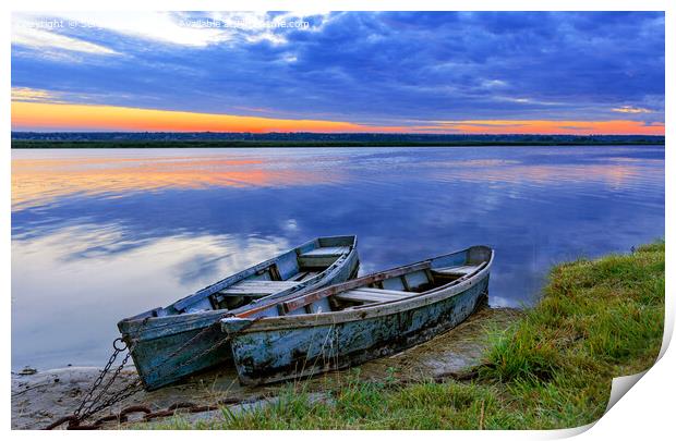 Two old blue-green boats moored by a metal chain to the shore of a calm river against the backdrop of the bright rising sun. Print by Sergii Petruk