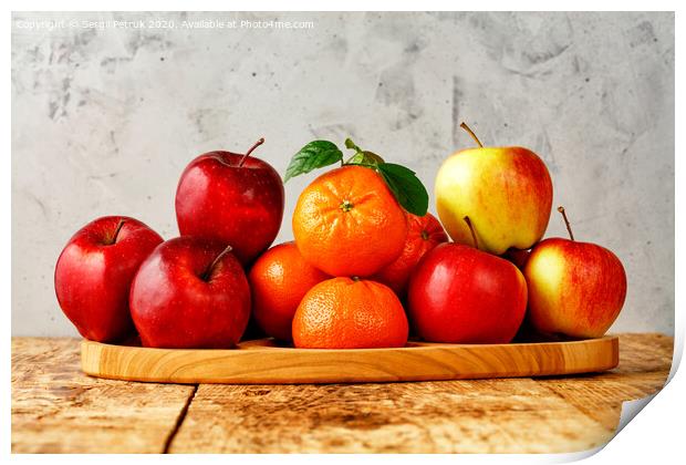 Red ripe apples and tangerines with green leaves lie on a wooden tray on an old wooden table with gray concrete background. Print by Sergii Petruk