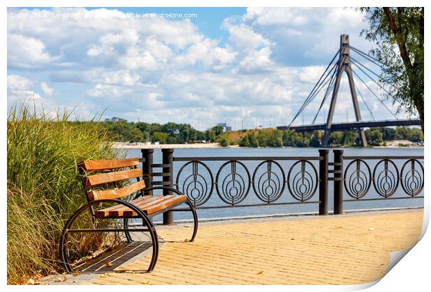 A wooden bench on the embankment of the Dnipro River against the background of yellow paving slabs and the northern bridge over the river in blur. Print by Sergii Petruk