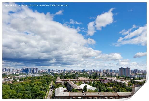 A cityscape with a green park in an old residential area of the city and new buildings on the horizon against a bright blue sky with thickening clouds. Print by Sergii Petruk