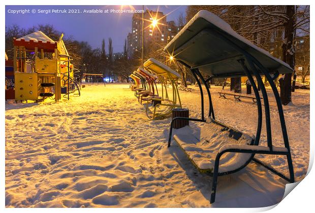 Wooden benches and a playground in the winter city evening park are covered with snow against the background of blue twilight. Print by Sergii Petruk