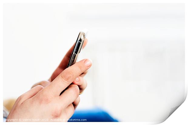 the hands of a young caucasian brunette woman while holding a smartphone typing on the touch screen. Print by Valerio Rosati