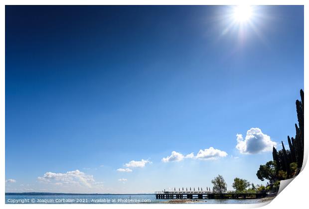 A strong sun illuminates the lake on a clear summer day, with sp Print by Joaquin Corbalan