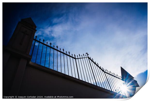 Metal grating of a cemetery with a cross on a white wall, copy space and deep and vibrant blue sky background. Print by Joaquin Corbalan
