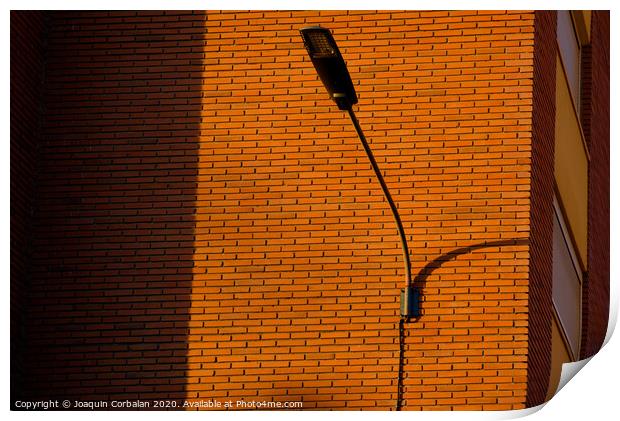 A deep red brick wall supports a lamppost, contrasting and bright colors. Print by Joaquin Corbalan