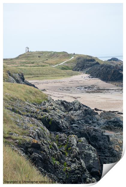 Rocky beach and lighthouse of Ynys Llanddwyn Print by Christopher Keeley