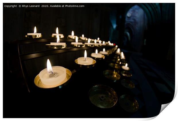 Prayer candles shine bright in a dark cathedral Print by Rhys Leonard