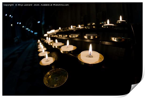 Prayer candles shine bright in a dark cathedral Print by Rhys Leonard