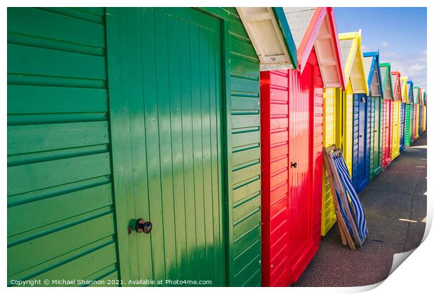 Colourful Beach Huts and a deck chair in Whitby Print by Michael Shannon