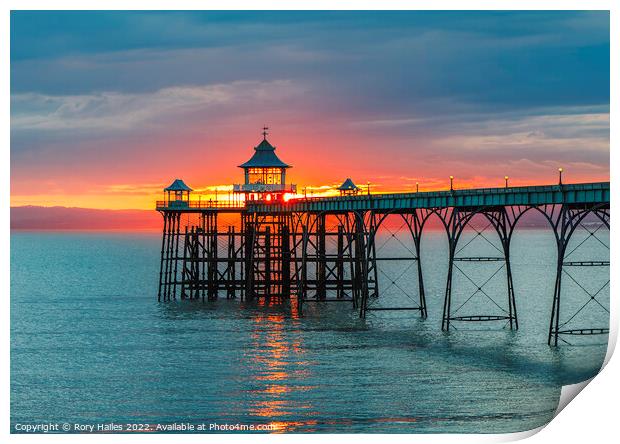 Clevedon Pier at sunset with a reddish orangey glow in the background Print by Rory Hailes