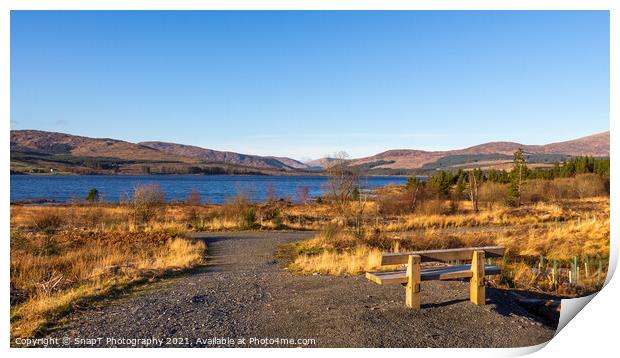 A wooden bench overlooking Clatteringshaws Loch on a sunny winters day Print by SnapT Photography