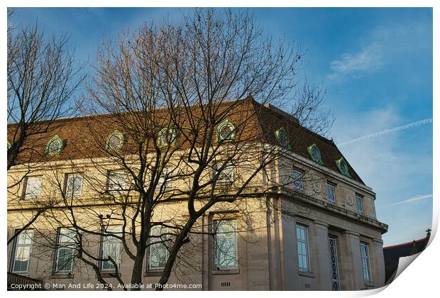 Classic European building facade with bare tree branches against a clear blue sky at dusk. Print by Man And Life