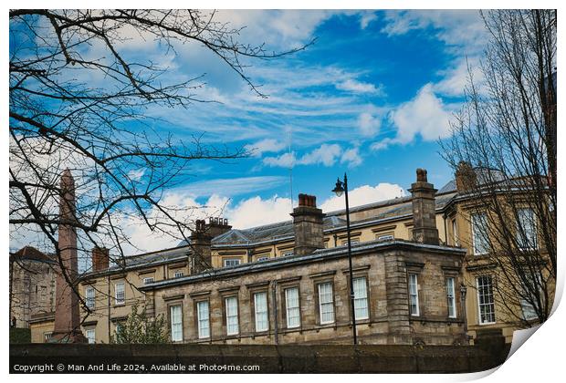 Classic European architecture with ornate details under a vibrant blue sky with fluffy clouds, framed by bare tree branches on the left in York, North Yorkshire, England. Print by Man And Life