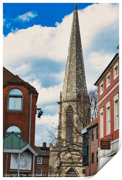 Vertical shot of an ancient church spire reaching into a blue sky with clouds, flanked by traditional brick buildings, showcasing architectural contrast and historical cityscape in York, North Yorkshire, England. Print by Man And Life