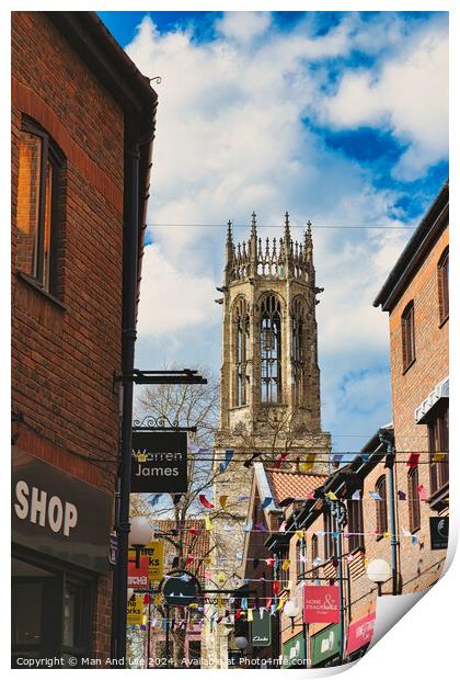 Quaint urban street with festive bunting leading to a historic church tower under a blue sky with fluffy clouds in York, North Yorkshire, England. Print by Man And Life