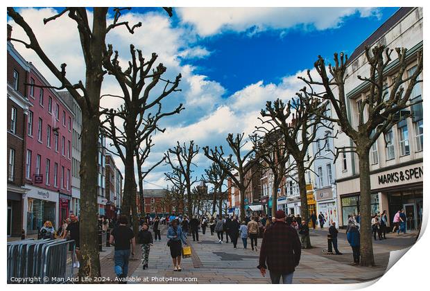 Vibrant city street bustling with pedestrians, lined with leafless pruned trees against a dynamic blue sky with fluffy clouds, showcasing urban life and seasonal change in York, North Yorkshire, England. Print by Man And Life