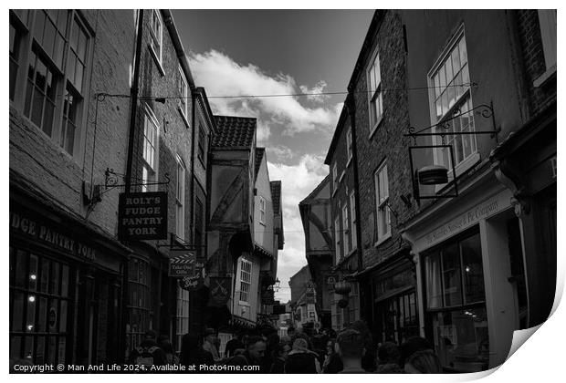 Black and white image of a bustling narrow street in York, with historic buildings, quaint shops, and pedestrians exploring the charming old town in York, North Yorkshire, England. Print by Man And Life