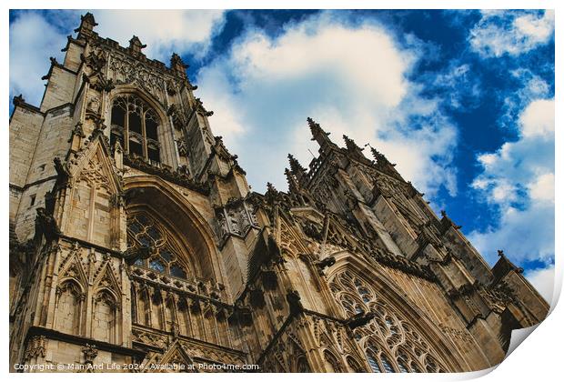 Dramatic angle of a Gothic cathedral's facade with intricate stone carvings against a vivid blue sky with fluffy clouds, showcasing architectural grandeur and historical elegance in York, North Yorkshire, England. Print by Man And Life