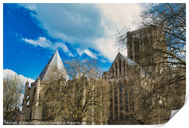 Historic medieval cathedral with Gothic architecture, featuring pointed arches and robust stone walls, set against a vibrant blue sky with fluffy clouds in York, North Yorkshire, England. Print by Man And Life