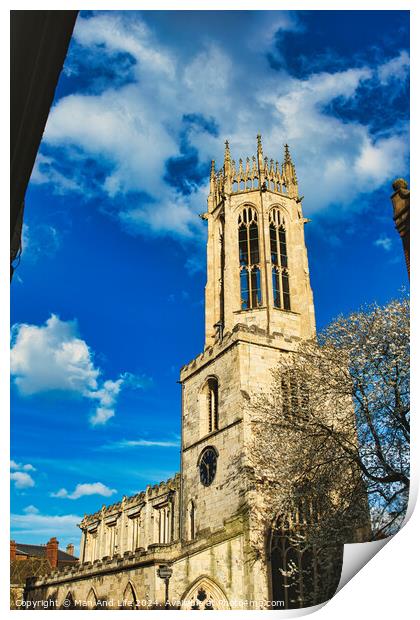 Gothic church tower against a vibrant blue sky with fluffy clouds, showcasing intricate architectural details and a blooming tree at the corner in York, North Yorkshire, England. Print by Man And Life