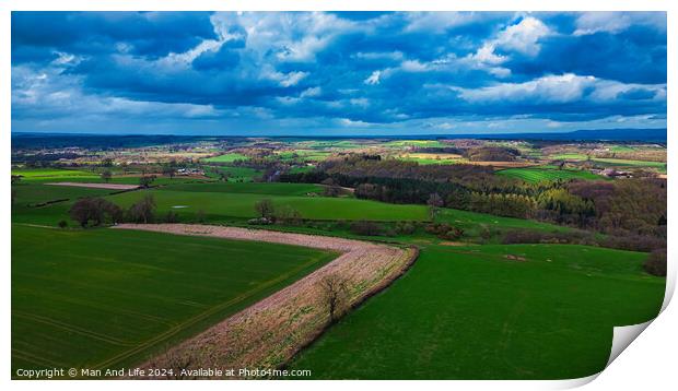 Vibrant aerial view of a lush countryside with patchwork fields under a dramatic sky, showcasing the beauty of rural landscapes and the diversity of agriculture. Print by Man And Life