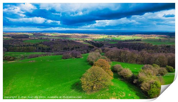 Vibrant aerial landscape with lush green fields, scattered trees, and a dramatic sky with fluffy clouds casting shadows over the countryside. Print by Man And Life